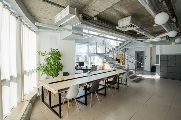 Modern office workspace with long meeting table, chairs, staircase, and industrial ceiling